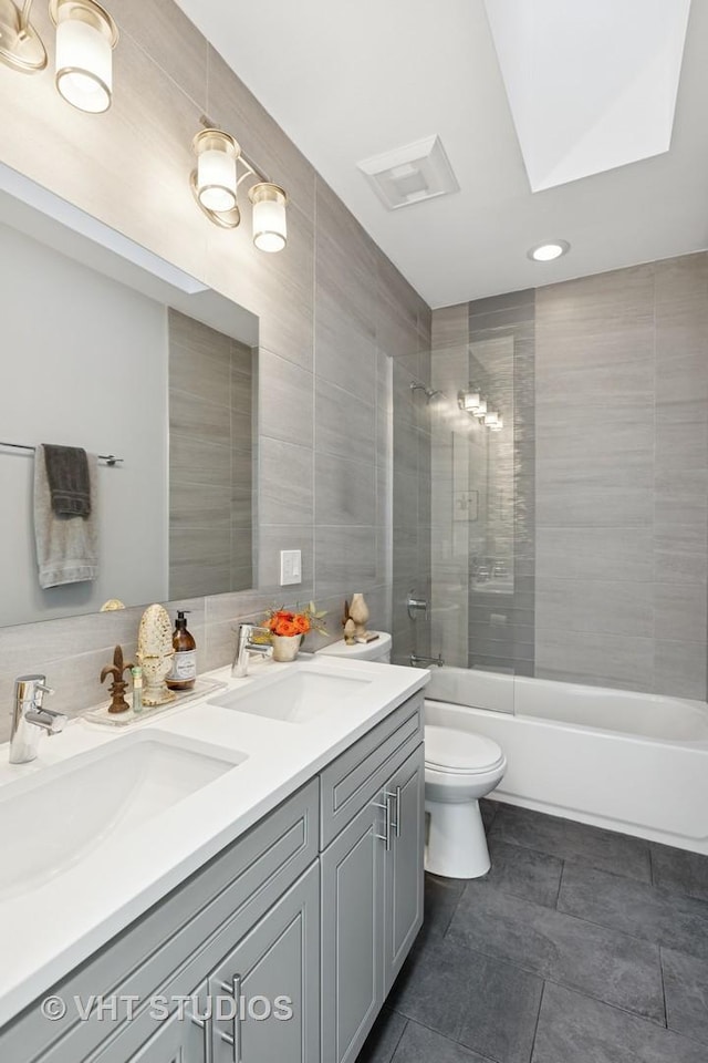 bathroom with toilet, washtub / shower combination, tile walls, and a sink