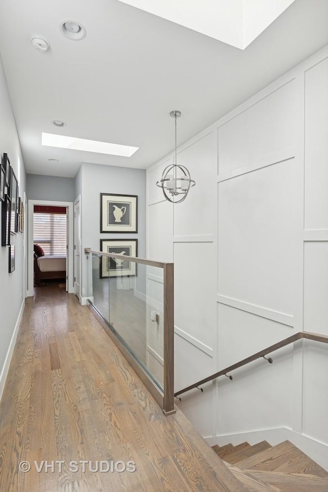 corridor featuring a skylight, an upstairs landing, wood finished floors, and baseboards