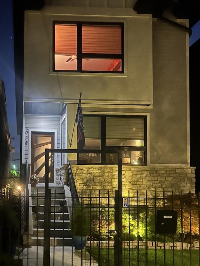 view of front of home featuring stone siding, stucco siding, stairs, and fence