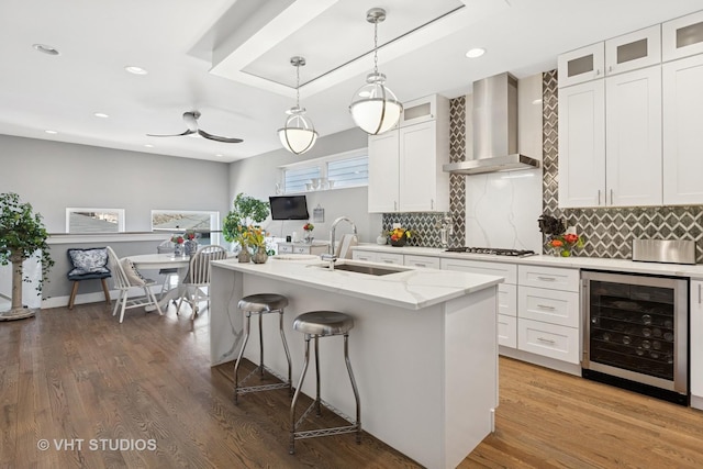 kitchen featuring wine cooler, white cabinets, wall chimney exhaust hood, and a sink