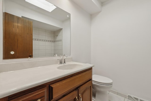 bathroom featuring toilet, a skylight, vanity, visible vents, and a tile shower