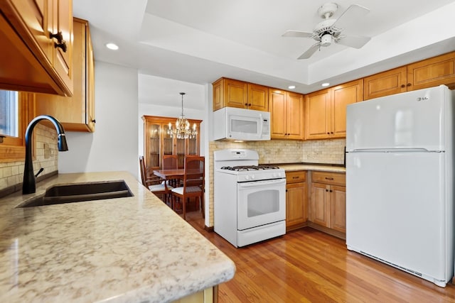 kitchen featuring light stone counters, light wood-style flooring, white appliances, a sink, and a tray ceiling