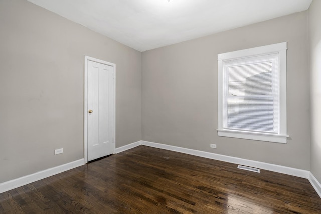 empty room featuring dark wood-style floors, visible vents, and baseboards