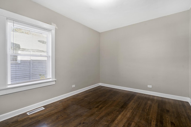 spare room with dark wood-style floors, visible vents, and baseboards