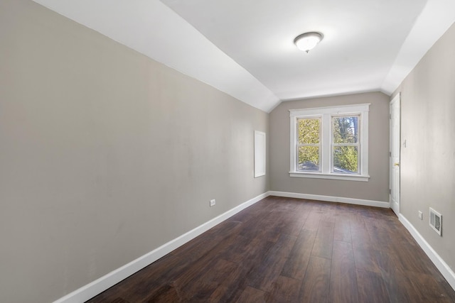 unfurnished room with dark wood-type flooring, lofted ceiling, visible vents, and baseboards