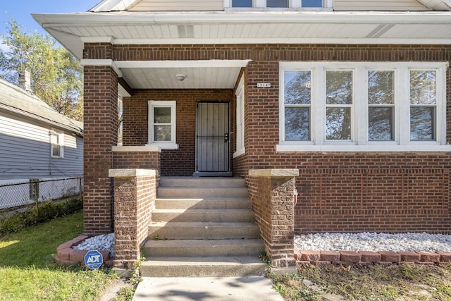 view of exterior entry with brick siding and fence