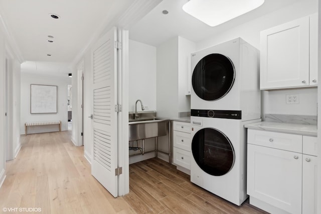 laundry room featuring cabinet space, a sink, light wood finished floors, and stacked washing maching and dryer