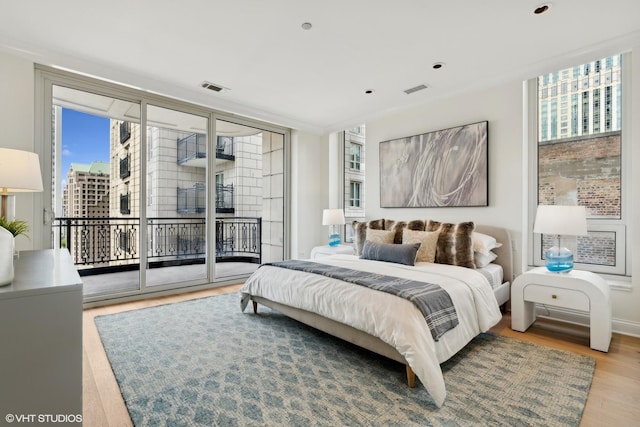 bedroom with access to outside, visible vents, a city view, and wood finished floors