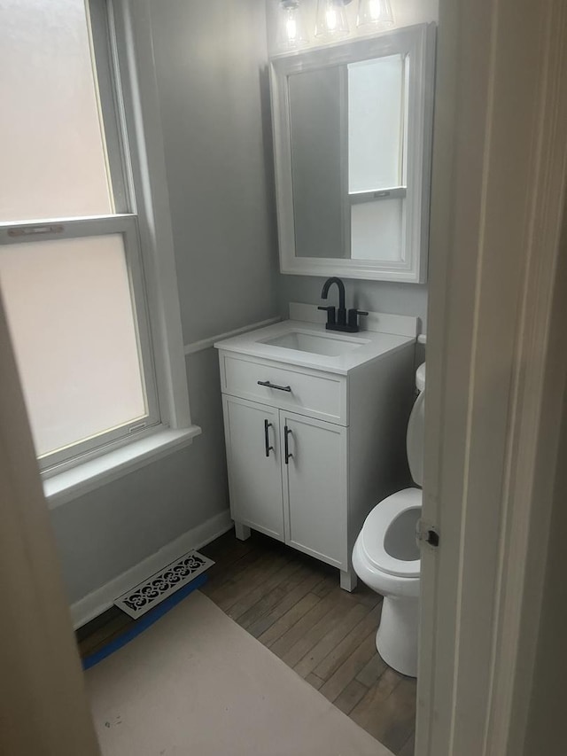 half bath with visible vents, vanity, toilet, and wood finished floors