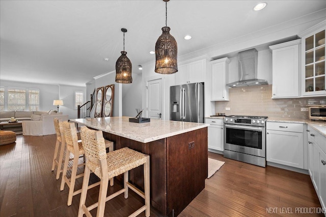 kitchen featuring appliances with stainless steel finishes, glass insert cabinets, white cabinets, a kitchen island, and wall chimney range hood