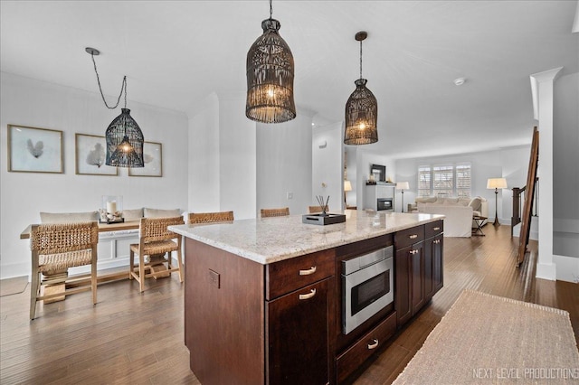 kitchen with stainless steel microwave, open floor plan, dark wood-style flooring, a center island, and hanging light fixtures