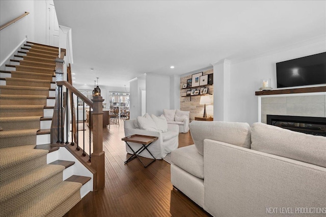 living area featuring dark wood-style floors, stairway, a tiled fireplace, and crown molding