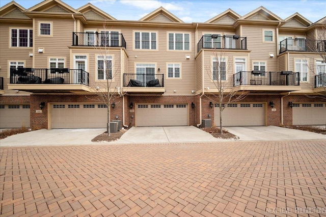 view of property with a garage, driveway, brick siding, and central AC