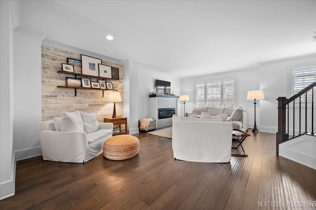 living area featuring dark wood-style flooring, a tiled fireplace, an accent wall, baseboards, and stairs