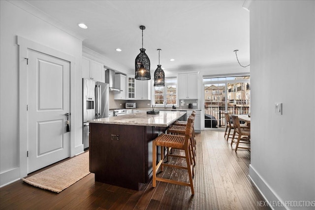 kitchen with high end refrigerator, a kitchen island, wall chimney range hood, light stone countertops, and glass insert cabinets