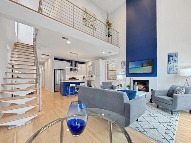 living area with a high ceiling, visible vents, stairway, light wood finished floors, and a glass covered fireplace