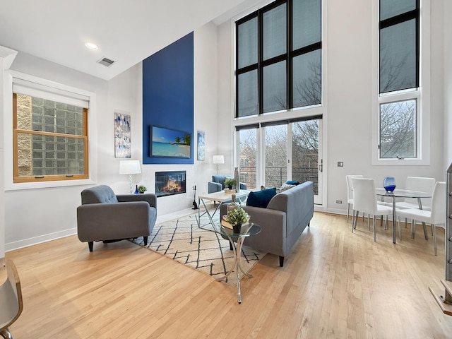 living room featuring baseboards, visible vents, a towering ceiling, wood-type flooring, and a fireplace