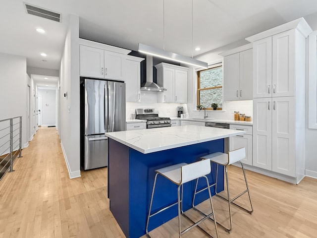 kitchen with stainless steel appliances, a kitchen island, visible vents, wall chimney range hood, and light wood-type flooring