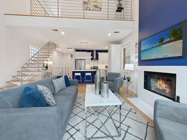 living area with light wood-style flooring, stairs, visible vents, and a tile fireplace