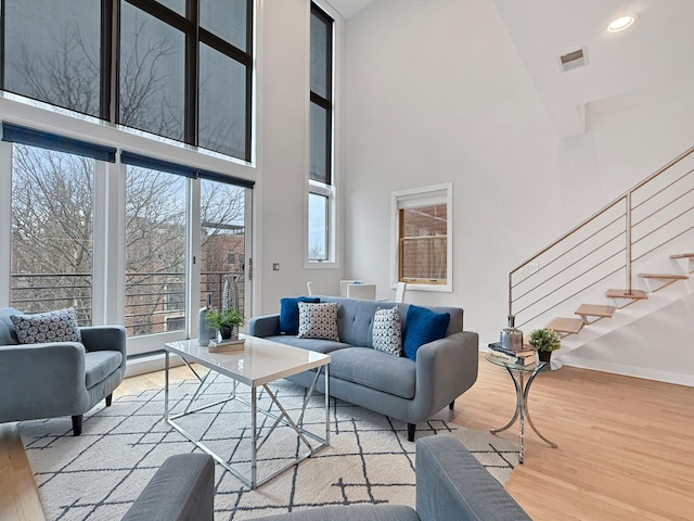 living area with visible vents, stairway, a towering ceiling, wood finished floors, and baseboards