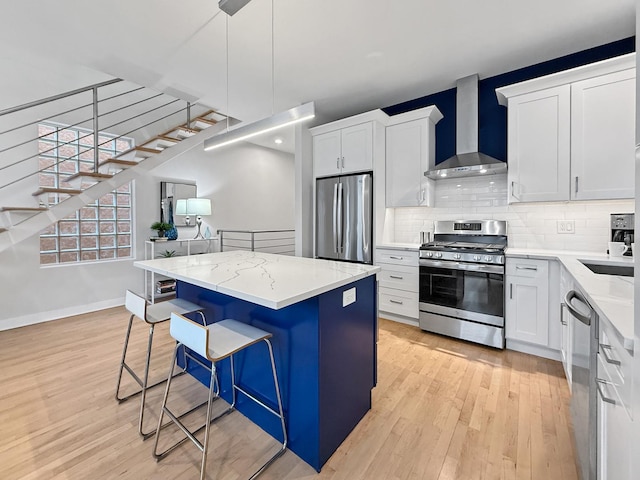 kitchen featuring wall chimney exhaust hood, tasteful backsplash, appliances with stainless steel finishes, a kitchen island, and a kitchen breakfast bar