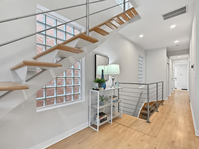 hallway featuring a wealth of natural light, wood finished floors, visible vents, and baseboards