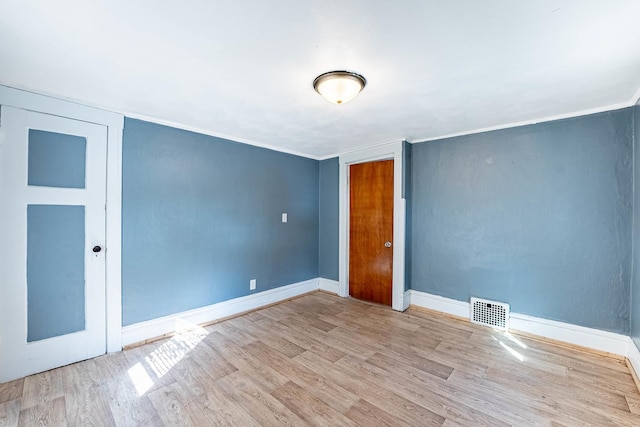 spare room with light wood-style floors, baseboards, visible vents, and ornamental molding