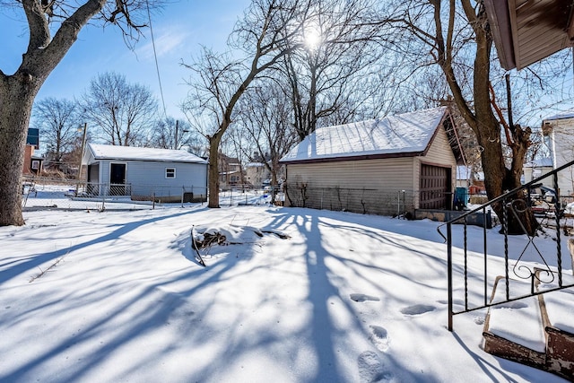 snowy yard with a garage, an outbuilding, and fence