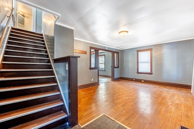 interior space with crown molding, baseboards, stairs, light wood-style floors, and ornate columns