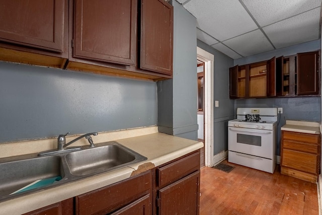 kitchen with light wood finished floors, white gas range oven, light countertops, a paneled ceiling, and a sink