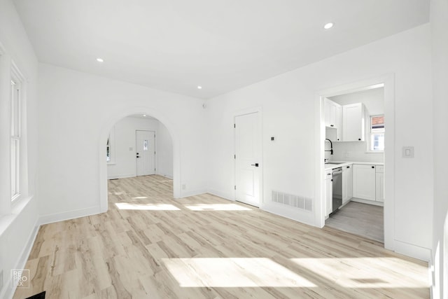 unfurnished room with arched walkways, light wood finished floors, visible vents, and recessed lighting