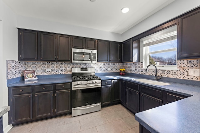 kitchen with light tile patterned flooring, a sink, appliances with stainless steel finishes, dark countertops, and backsplash