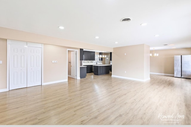 unfurnished living room with light wood-style floors, a chandelier, visible vents, and baseboards