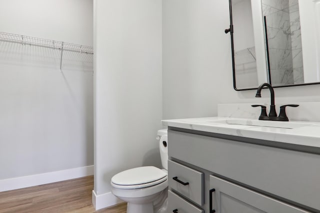 full bathroom with a walk in closet, toilet, vanity, wood finished floors, and baseboards