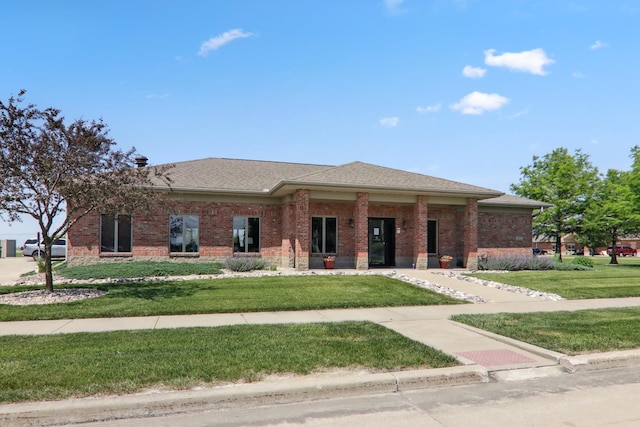 view of front facade featuring a shingled roof, a front yard, and brick siding