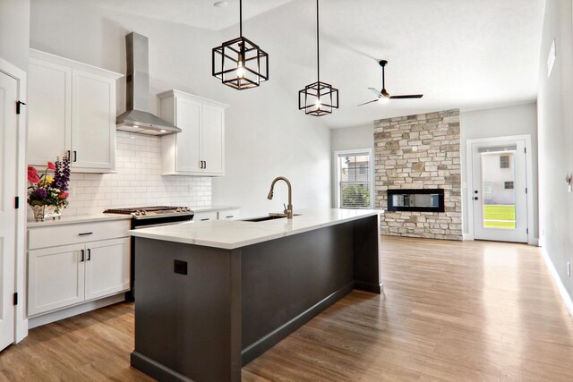 kitchen featuring light stone counters, hanging light fixtures, open floor plan, white cabinets, and wall chimney range hood
