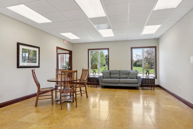 dining space with a drop ceiling, light tile patterned flooring, and baseboards