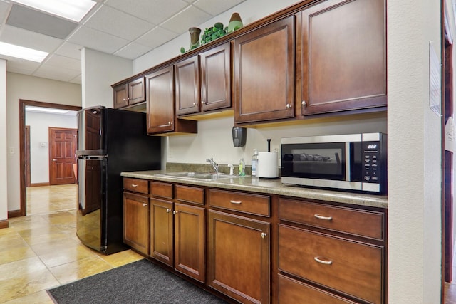 kitchen with a paneled ceiling, dark countertops, stainless steel microwave, freestanding refrigerator, and a sink