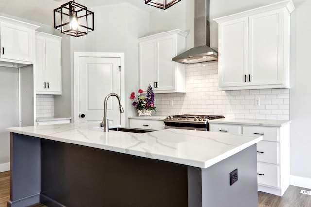 kitchen featuring a center island with sink, gas stove, white cabinetry, a sink, and wall chimney exhaust hood