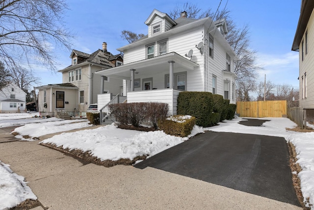 view of front of house featuring covered porch, a chimney, and fence