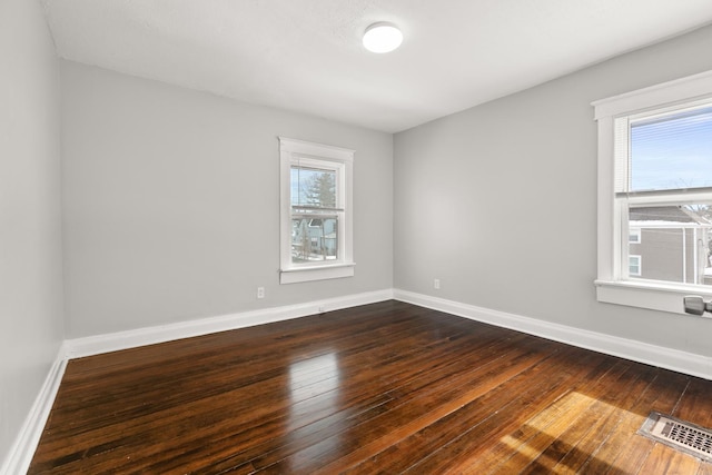 spare room with wood finished floors, visible vents, and baseboards