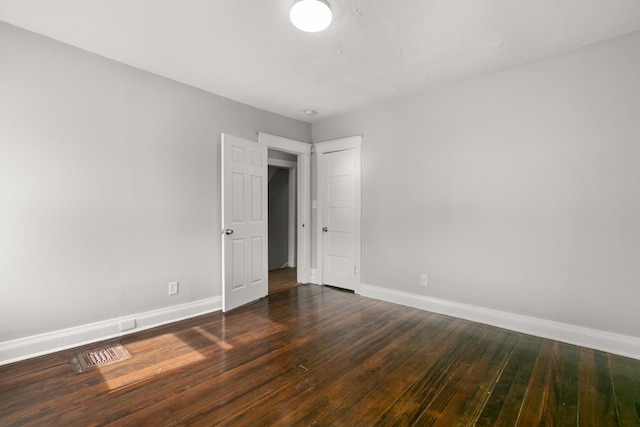 empty room featuring dark wood-type flooring, visible vents, and baseboards