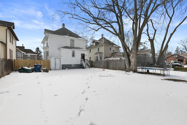 snow covered house featuring a trampoline, a residential view, and fence