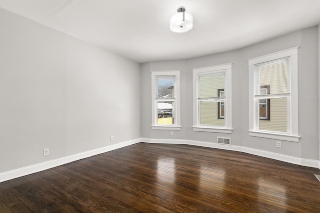 spare room with dark wood-style floors, visible vents, and baseboards