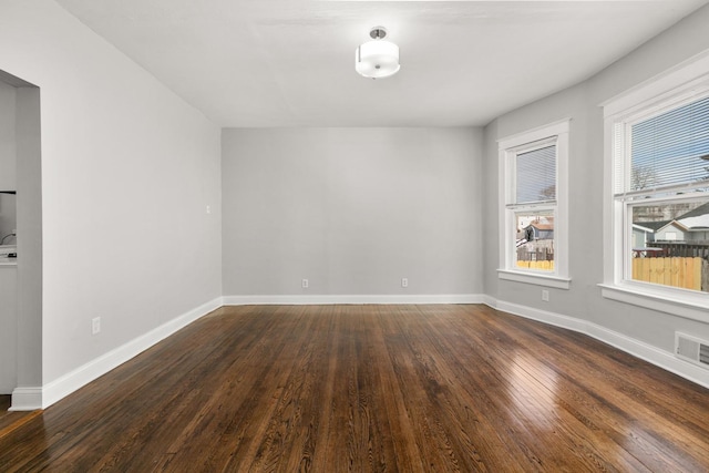 unfurnished room with dark wood-style flooring, visible vents, and baseboards