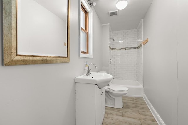 bathroom with visible vents, toilet, vanity, wood finish floors, and shower / washtub combination