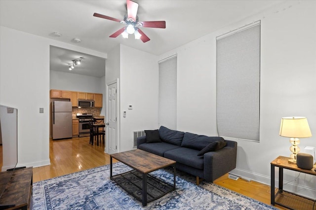 living area with light wood finished floors, visible vents, baseboards, and a ceiling fan