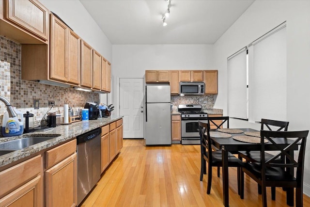 kitchen with light stone counters, a sink, appliances with stainless steel finishes, light wood-type flooring, and tasteful backsplash