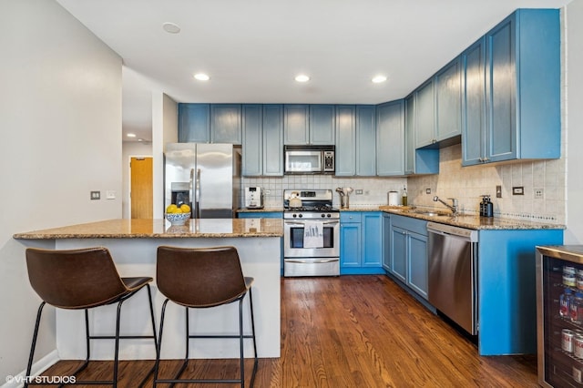 kitchen featuring light stone counters, appliances with stainless steel finishes, dark wood-type flooring, blue cabinets, and beverage cooler