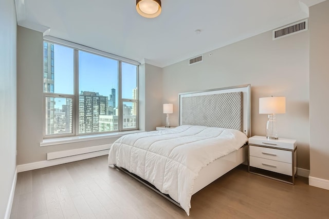 bedroom with a view of city, wood finished floors, visible vents, and baseboards